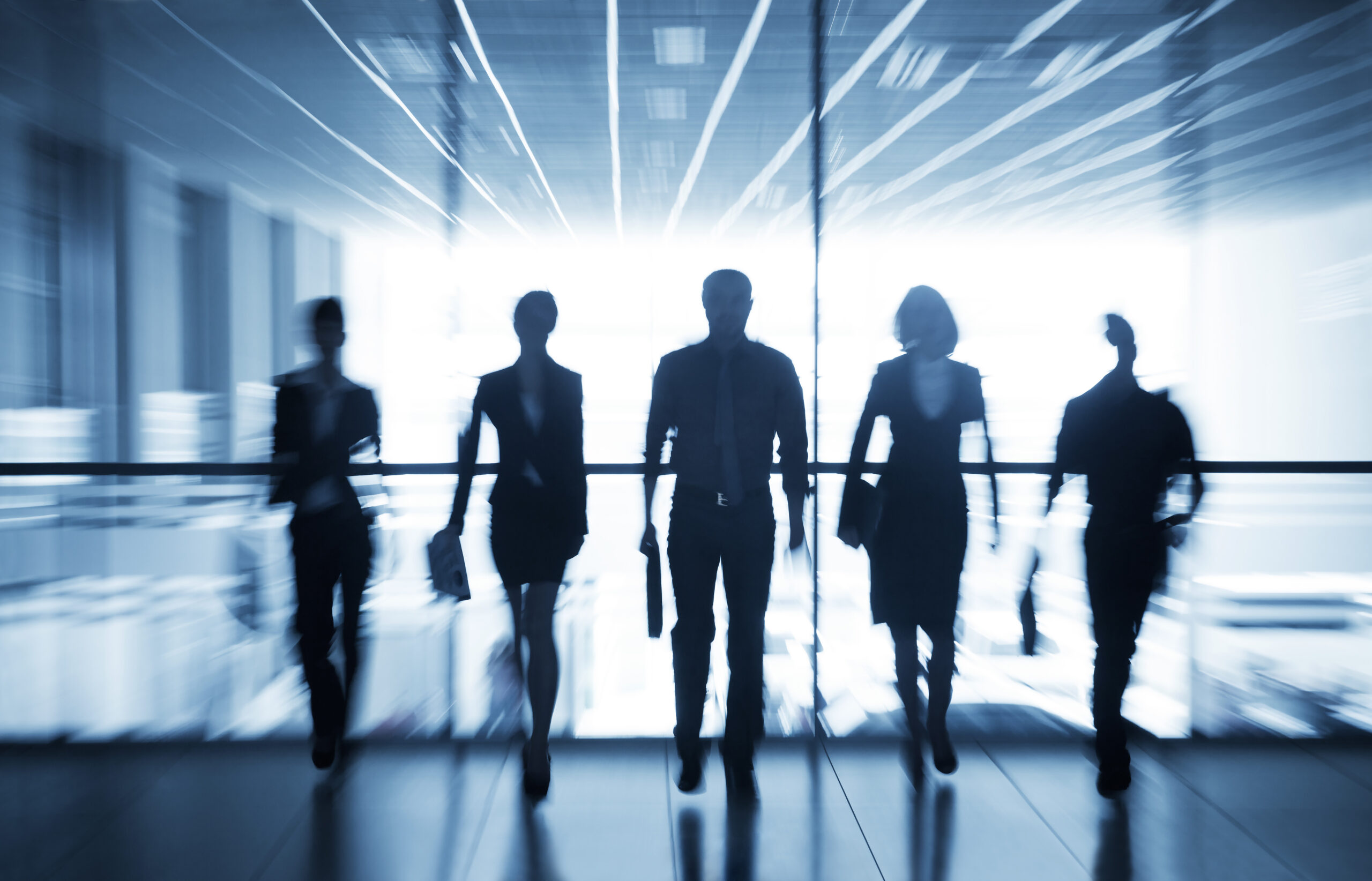 Five professional male and female consultants walking into an office space with a blurred background.